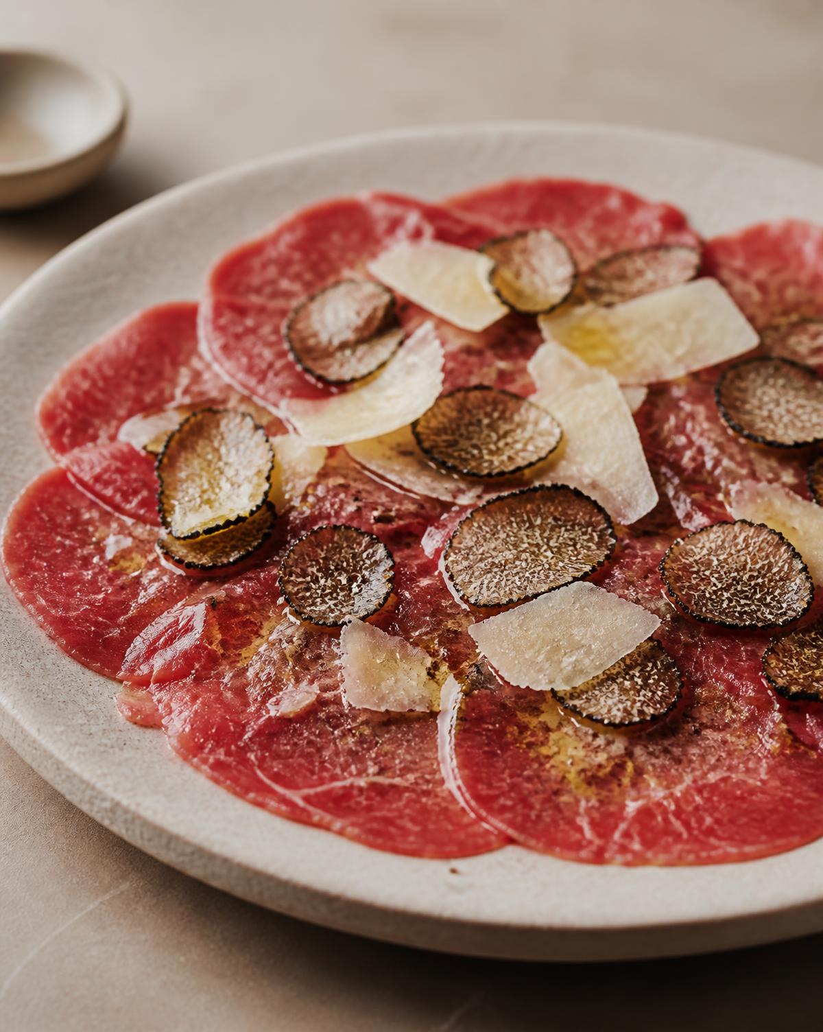 Carpaccio di manzo con scaglie di Parmigiano e tartufo nero su piatto in ceramica